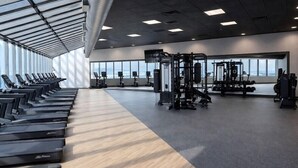 Ett gym med löpband, styrketräningsmaskiner och ett stort fönster.