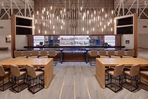 Un espace bar moderne doté d’un long comptoir, de nombreux sièges et d’un luminaire suspendu original.