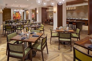 A hotel dining area with multiple tables and chairs, a buffet counter, and a large mural on the wall. - Nashville Airport Marriott (Nashville)