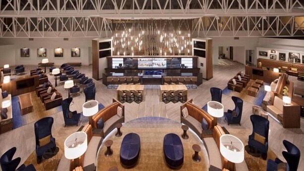En rymlig entréhall med en central bar, flera sittgrupper och ett högt tak med ett geometriskt mönster.