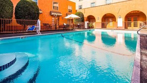 A swimming pool with lounge chairs and umbrellas, surrounded by a building with arched doorways and a tiled floor. - Motel6 Dallas, TX - Downtown (Dallas)