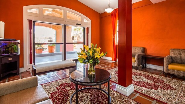 A room with a curved glass door, a round table with a vase of yellow flowers, a red pillar, and patterned rugs. - Motel6 Dallas, TX - Downtown (Dallas)