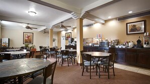 A restaurant with multiple dining tables and chairs, a kitchen area with appliances, and ceiling fans. - Motel6 Dallas, TX - Downtown (Dallas)