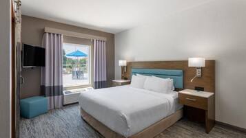 A hotel room with a bed, a television, a window with curtains, a nightstand, and a lamp.