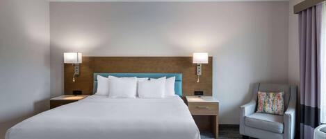 Habitación de hotel con una cama grande, dos mesitas de noche, una silla y un cabecero con lámparas de pared.