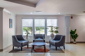 A lobby with three grey armchairs, a round table, large windows, and potted plants. - Tryp by Wyndham Tallahassee North I-10 Capital Cir (Tallahassee)