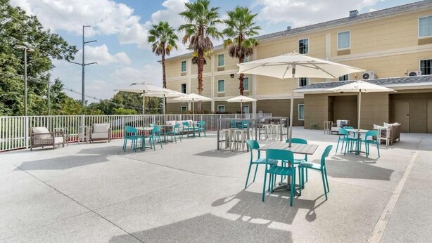 An outdoor patio area with tables and chairs, palm trees, and a building in the background. - Tryp by Wyndham Tallahassee North I-10 Capital Cir (Tallahassee)