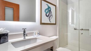 A bathroom with a white sink, a mirror, a framed abstract painting, and a glass shower enclosure. - Tryp by Wyndham Tallahassee North I-10 Capital Cir (Tallahassee)