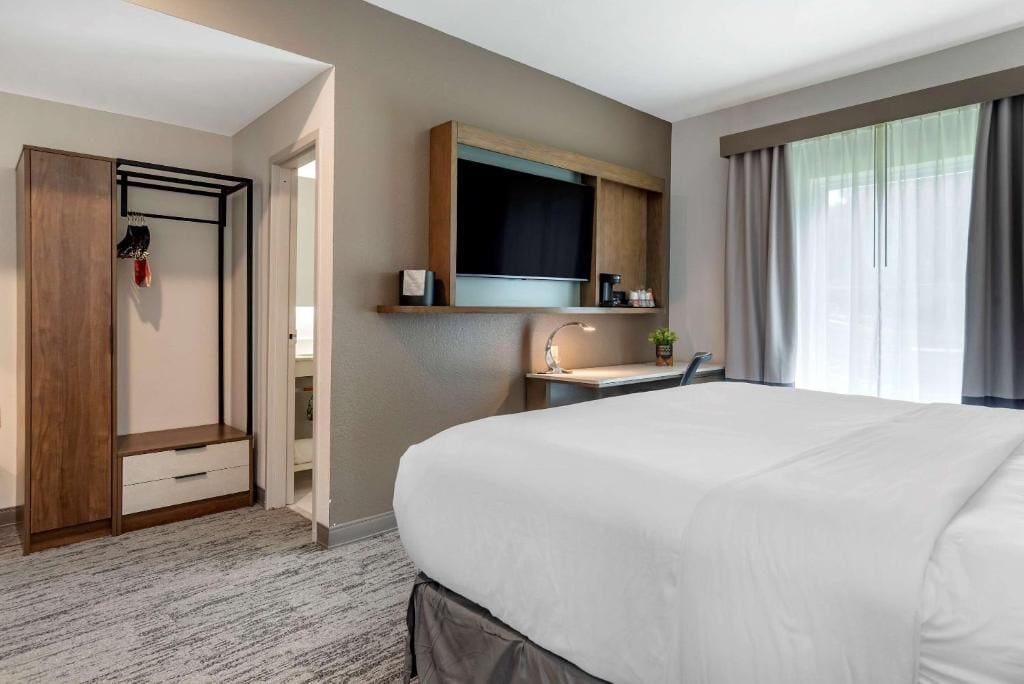 A hotel room with a bed, a wardrobe, a vanity with a mirror, and a window with curtains.
