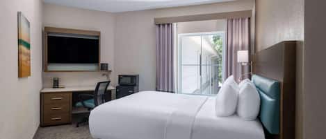 A hotel room with a bed, desk, chair, and a large window with curtains.