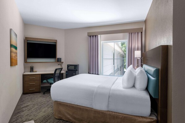 A hotel room with a bed, desk, chair, and a large window with curtains. - Tryp by Wyndham Tallahassee North I-10 Capital Cir (Tallahassee)