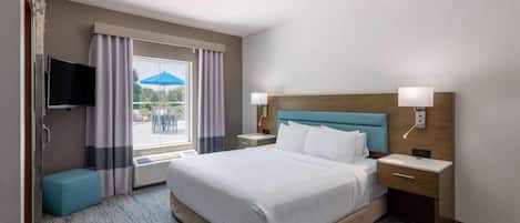 Quarto de hotel com uma cama grande, duas mesas de cabeceira, televisão e janela com cortinas.