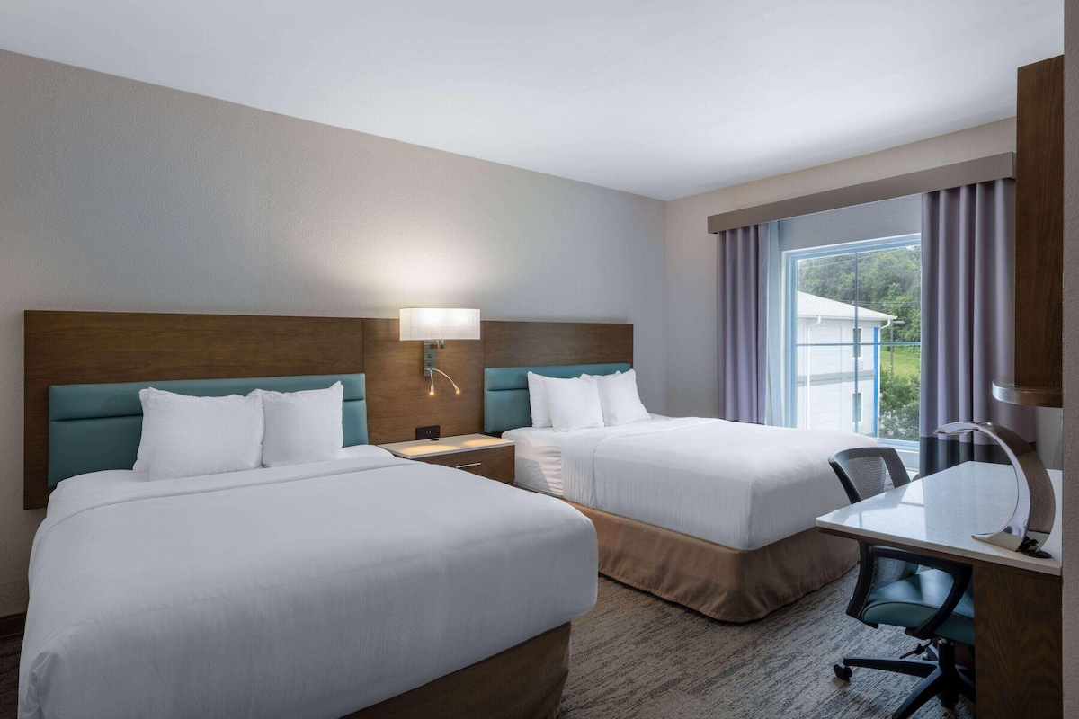 A hotel room with two beds, a desk, and a chair.