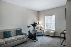 A room with a sofa, an exercise bike, a chair, a table, and a window with blinds. - Tryp by Wyndham Tallahassee North I-10 Capital Cir (Tallahassee)