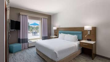 A hotel room with a large bed, two bedside tables, a TV, and a window with curtains.