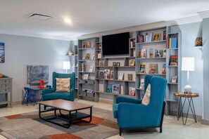 A living room with two teal armchairs, a coffee table, a flat-screen TV, and a bookshelf filled with books. - Tryp by Wyndham Tallahassee North I-10 Capital Cir (Tallahassee)