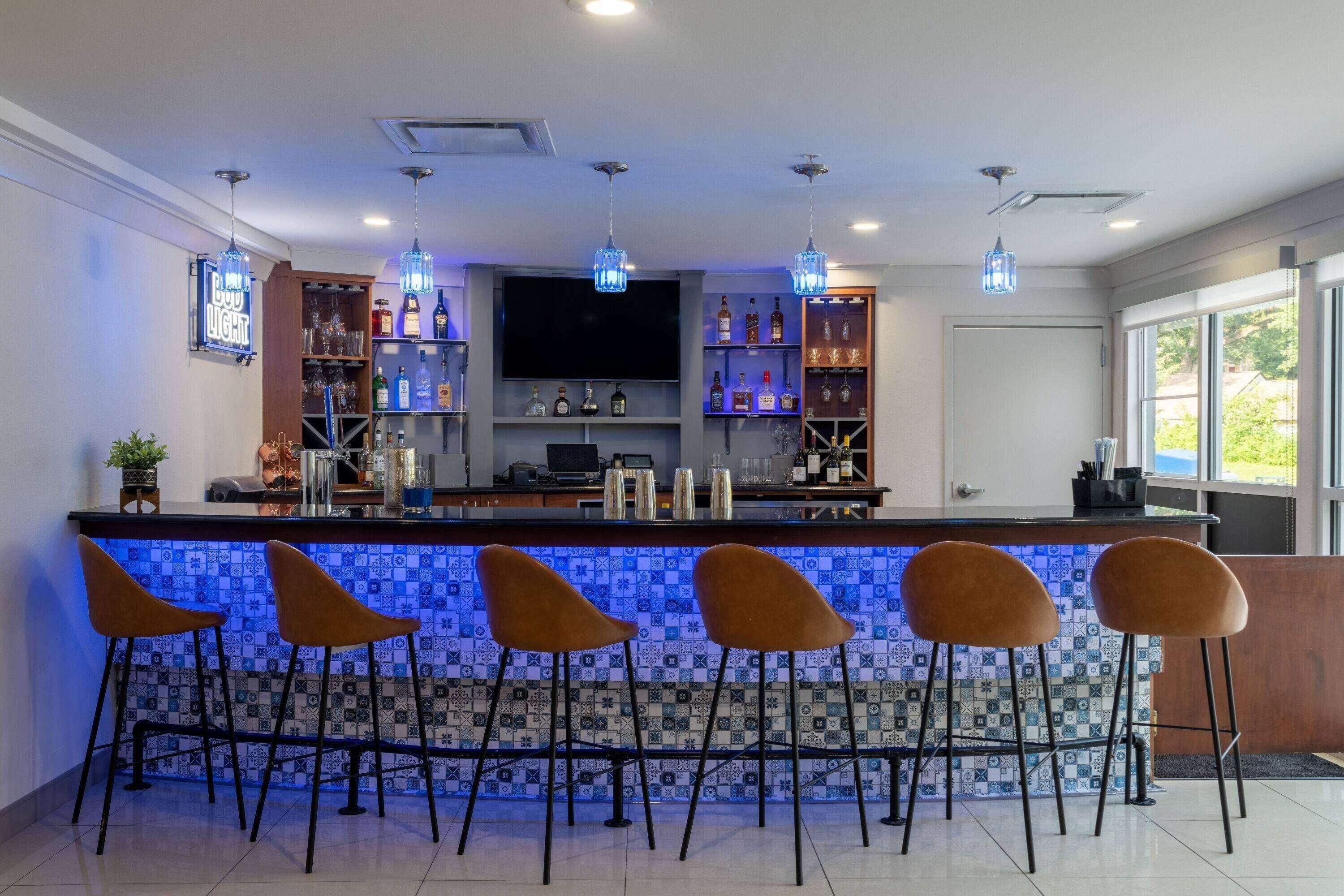 Un espace bar agrémenté d’un mur recouvert de carreaux, de tabourets de bar et d’une variété de bouteilles.