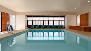 A swimming pool with a row of chairs, a ladder, and a windowed wall. - Wingate by Wyndham Williamsburg (Williamsburg)