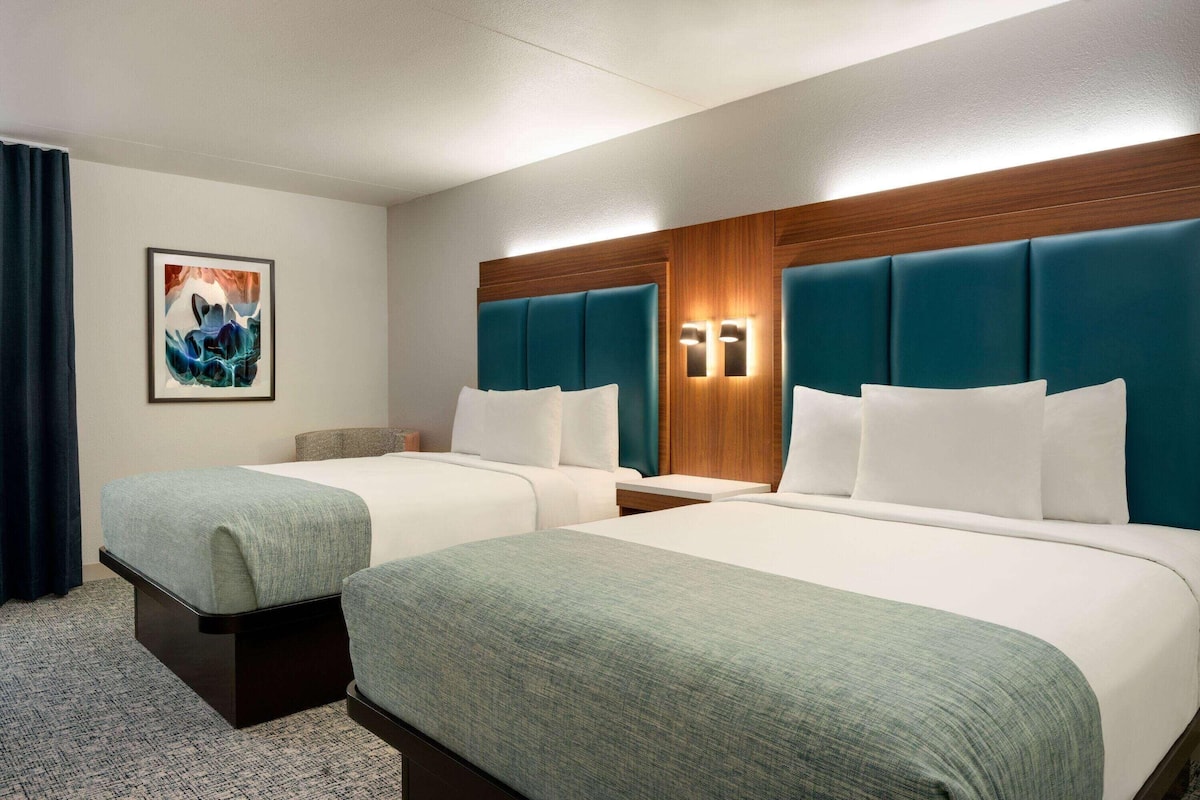 Hotellihuone, jossa on kaksi sänkyä, puinen pääty ja yöpöytä sekä taulu.