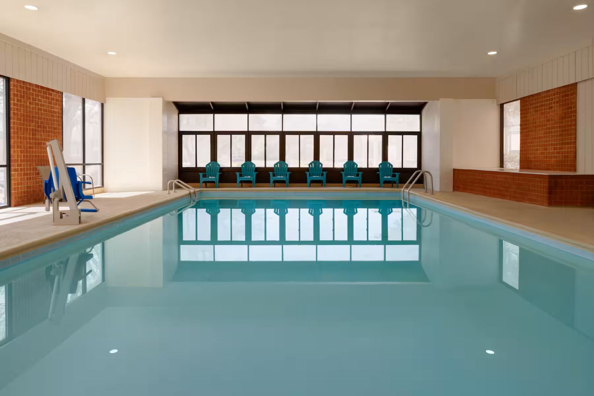 En swimmingpool med en række stole, en stige og en væg med vinduer.