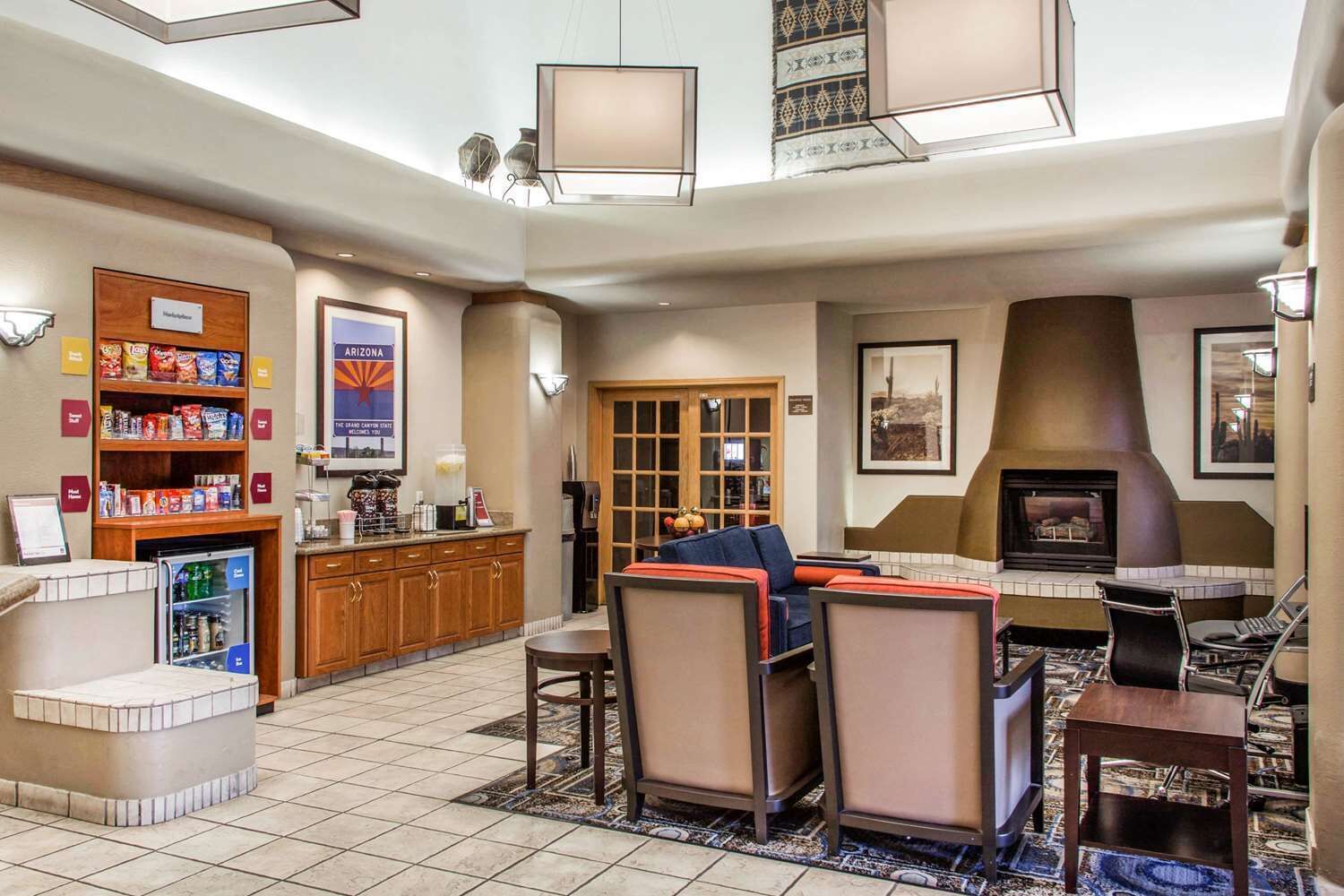 A hotel lobby with a seating area, a kitchenette, a refrigerator stocked with snacks, and a fireplace.