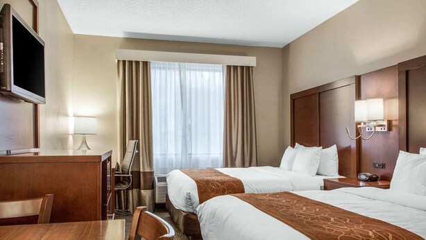Une chambre d’hôtel avec deux lits, un bureau, une télévision et une fenêtre avec des rideaux.