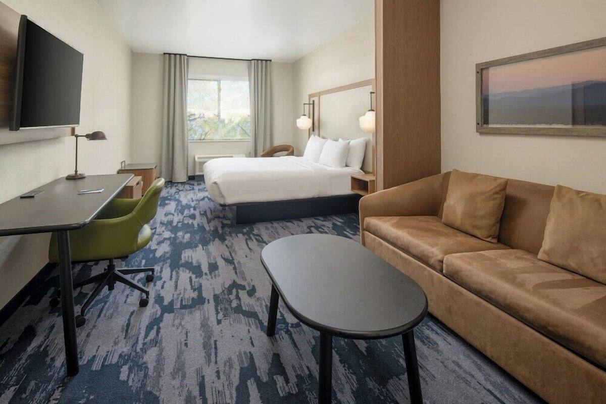 A hotel room with a bed, a sofa, a desk with a chair, a TV, and a window with curtains.
