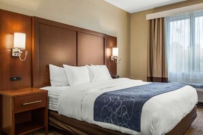 Habitación de hotel con una cama grande, dos lámparas de noche, una mesita de noche y un ventanal con cortinas.