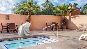 Un espace piscine avec des chaises longues et des tables, une table abritée et un panneau indiquant les règles du spa.