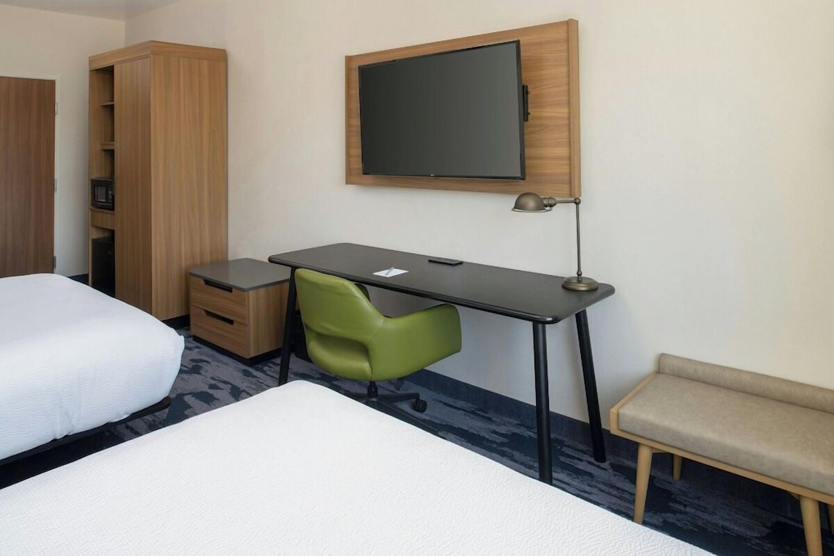 A hotel room with a bed, a desk with a chair, a television, and a wardrobe.