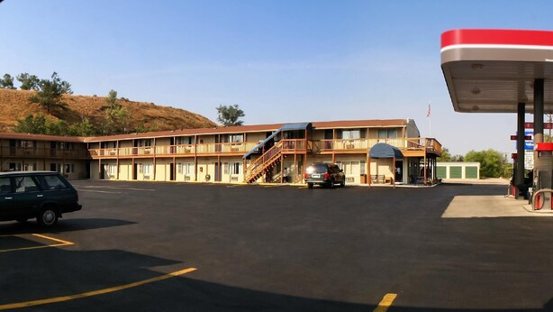 A motel with a parking lot, a gas station, and a hillside in the background. - Evergreen Studios (Sheridan)