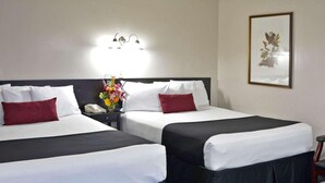 Two adjacent beds with white and black bedding, a nightstand with a telephone, a vase with flowers, and a framed picture on the wall. - Evergreen Studios (Sheridan)