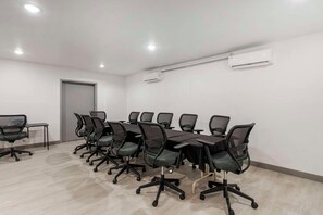 Een vergaderzaal met een lange tafel, stoelen, een airconditioner en een deur.
