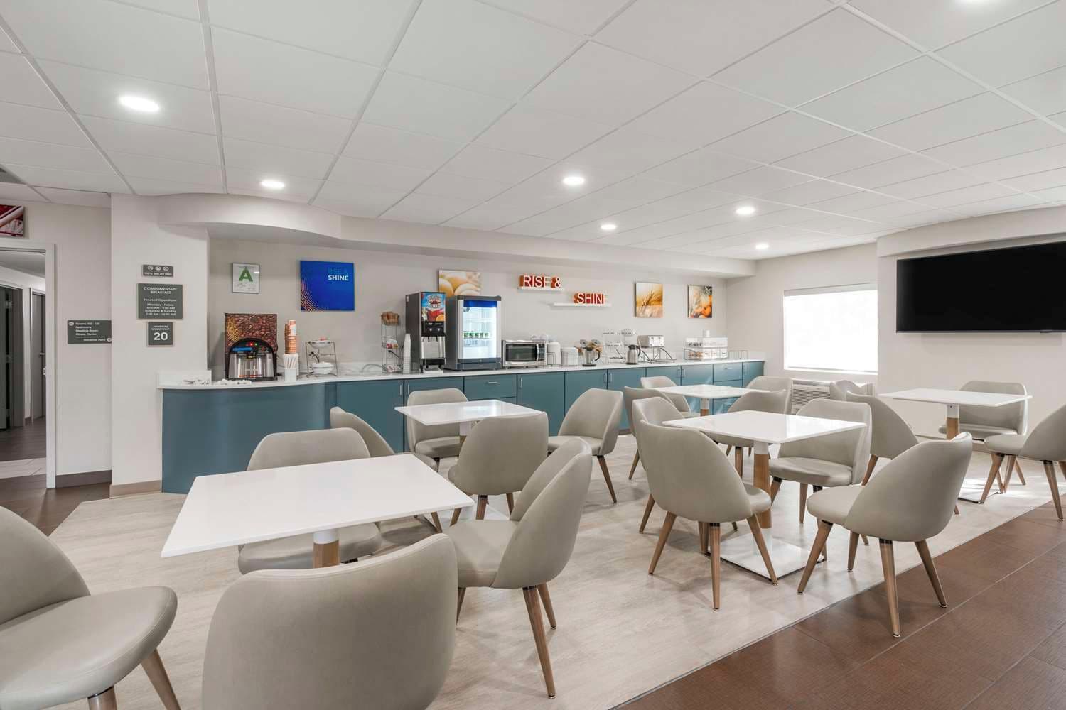 A modern dining area with tables and chairs, a counter with a coffee machine, and a TV mounted on the wall.