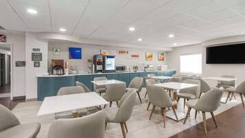 A modern dining area with tables and chairs, a counter with a coffee machine, and a TV mounted on the wall.