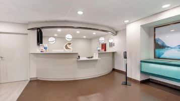A reception area with a curved desk, overhead lighting, a bench, and a wall-mounted screen.