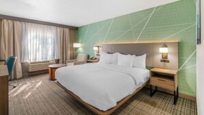 A hotel room with a large bed, a desk, a chair, a nightstand, and a wall-mounted lamp.