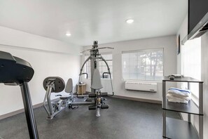 Una palestra con attrezzature per esercizi, un tapis roulant e una finestra con condizionatore.