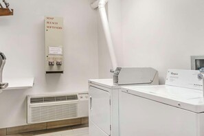 Locale lavanderia con lavatrice e asciugatrice Whirlpool, un sistema di ventilazione e un cartello che indica l'uso di ammorbidenti.