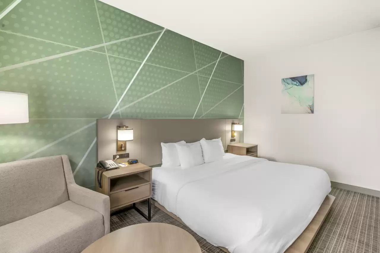 A hotel room with a large bed, a sofa, a desk with a lamp, and a small table.