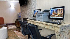 Un mostrador de recepción con dos monitores, una impresora y una caja registradora. Hay dos sillas y una pequeña mesa con un objeto decorativo.