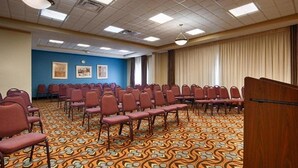 Un salón de conferencias con filas de sillas, una alfombra estampada y una pared azul con cuadros enmarcados.