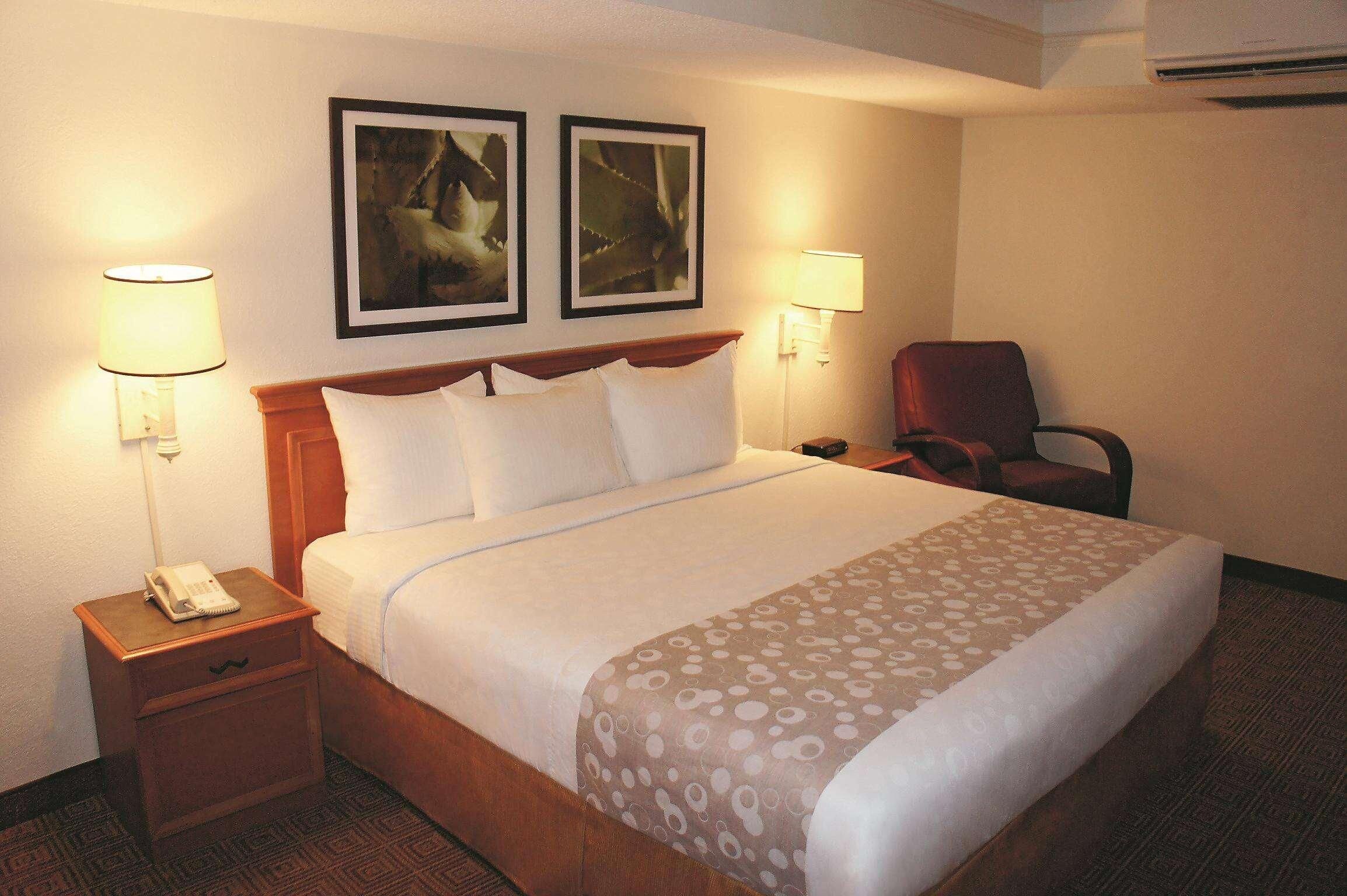 A hotel room with a bed, two wall-mounted lamps, a chair, and a telephone on a nightstand.
