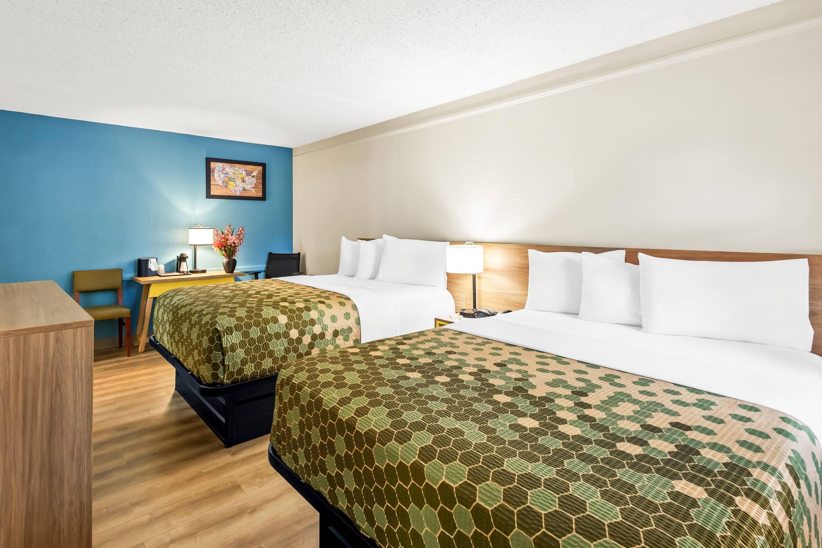Une chambre d’hôtel avec deux lits, un bureau, une chaise et une lampe.
