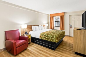 A hotel room with a bed, a red chair, a desk with a lamp, and a television. - Econo Lodge Augusta North - Washington Road (Augusta)