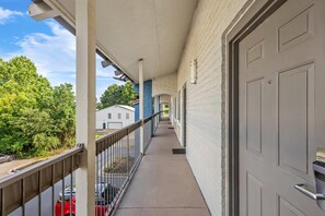 A covered balcony with a metal railing, a white door, and a view of a residential street. - Econo Lodge Augusta North - Washington Road (Augusta)