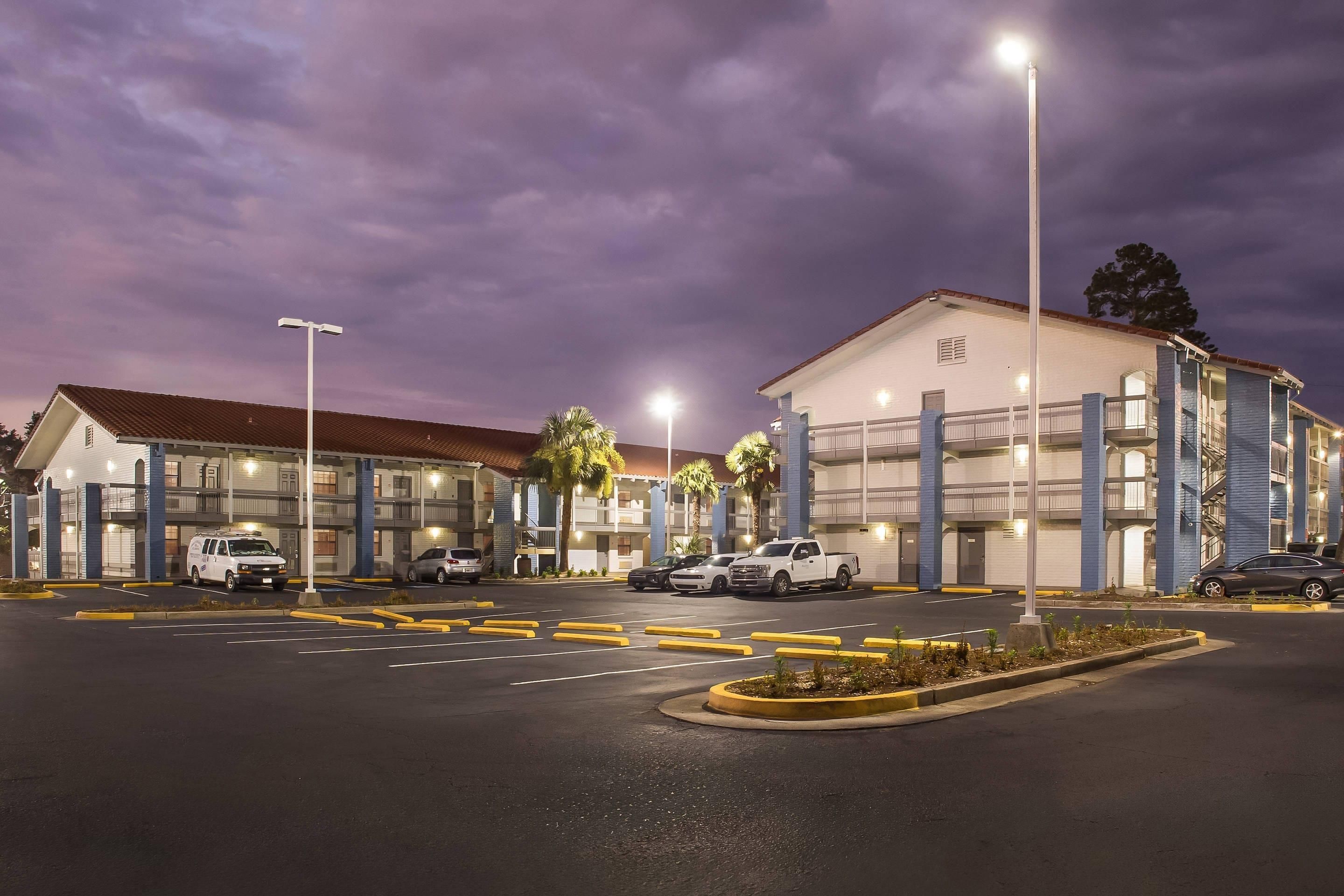 Un hotel con estacionamiento, varios vehículos y un edificio con techo rojo.