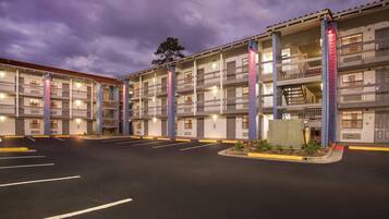 Un hotel de varios pisos con balcones, un estacionamiento y un cielo despejado.