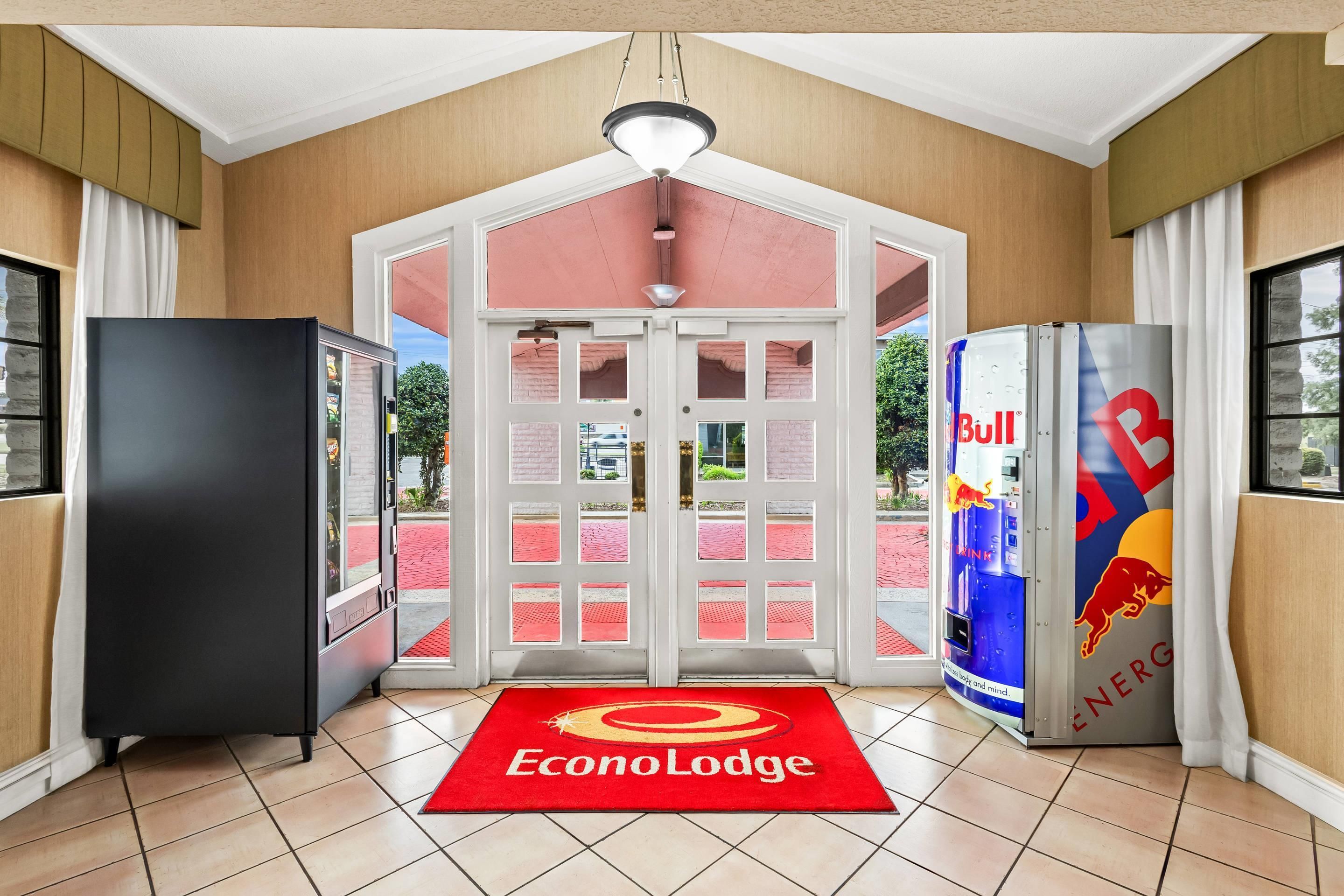 Entrada de hotel con alfombra roja, un refrigerador y una máquina expendedora de Red Bull.