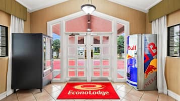 Entrada de hotel con alfombra roja, un refrigerador y una máquina expendedora de Red Bull.